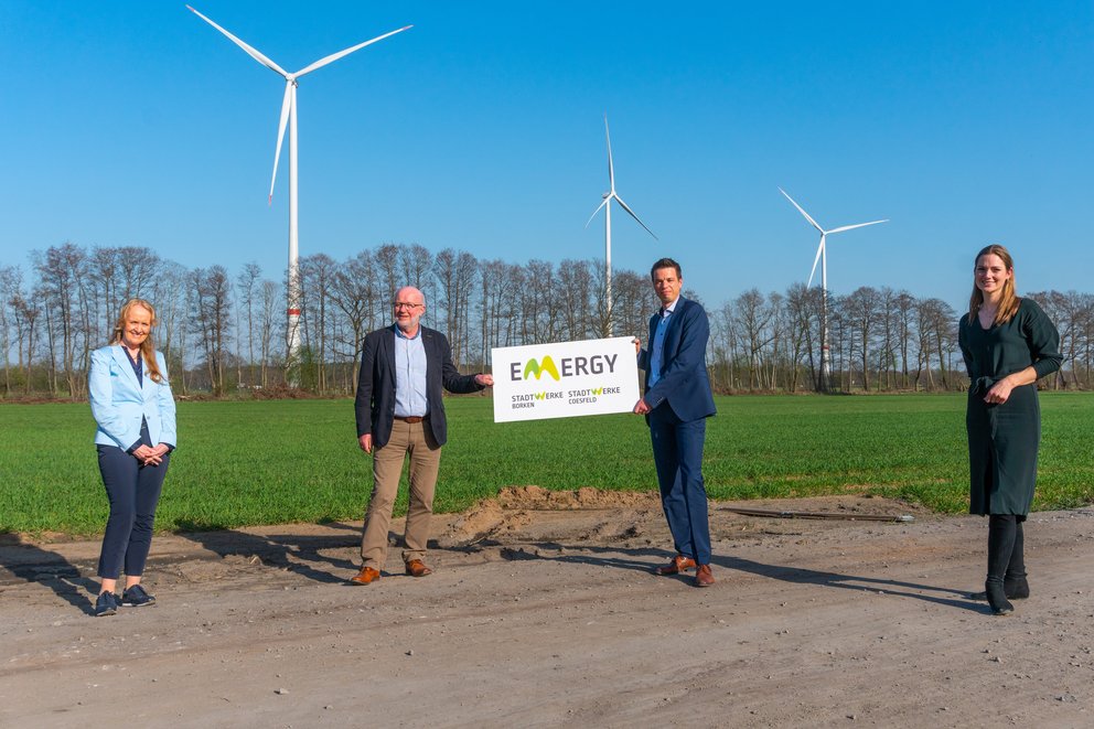 Eröffnung Windpark. vier Personen auf einem Feld mit Windrädern.