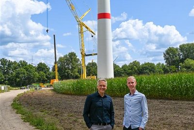  Personen auf einem Feldweg vor einem Baukran beim Aufbau einer Windkraftanlage