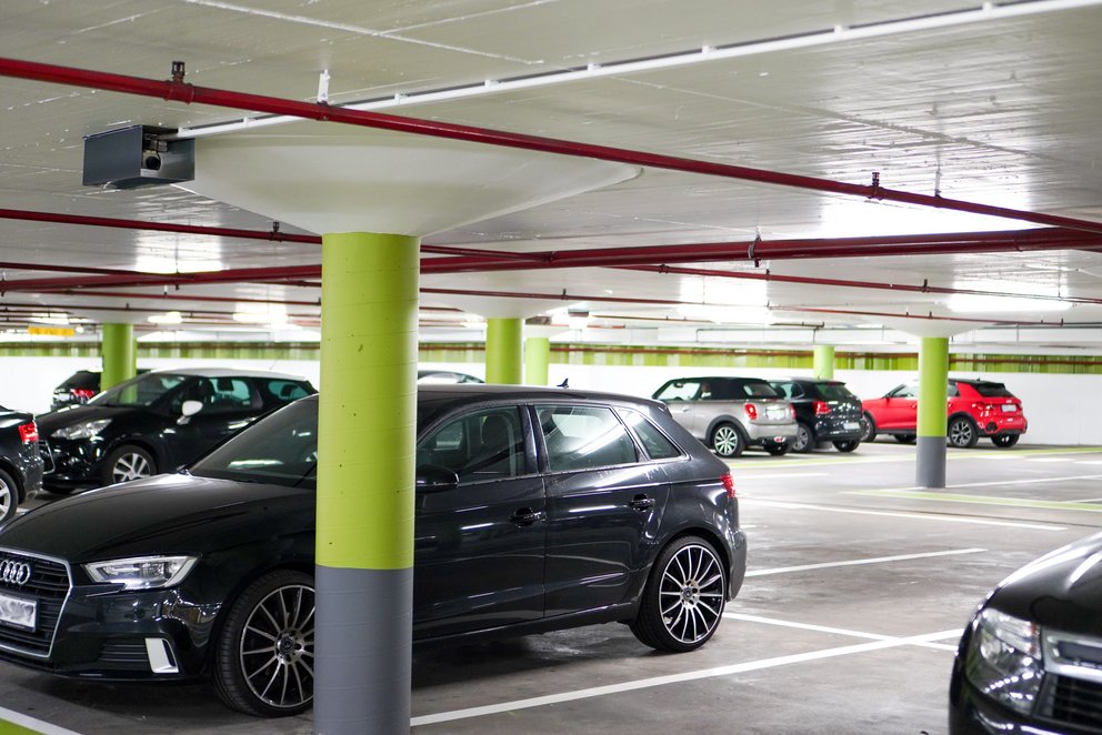Moderne und helle Tiefgarage mit parkenden Autos. Die Säulen sind grau/grün.