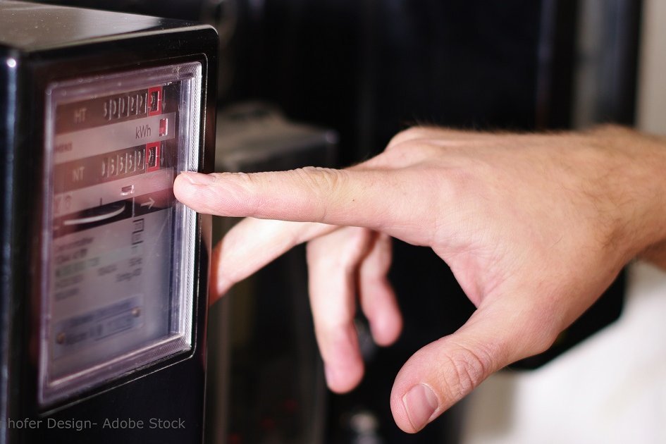 Person zeigt auf Stromzähler. Einer Person zeigt mit dem Finger auf einen Stromzähler.