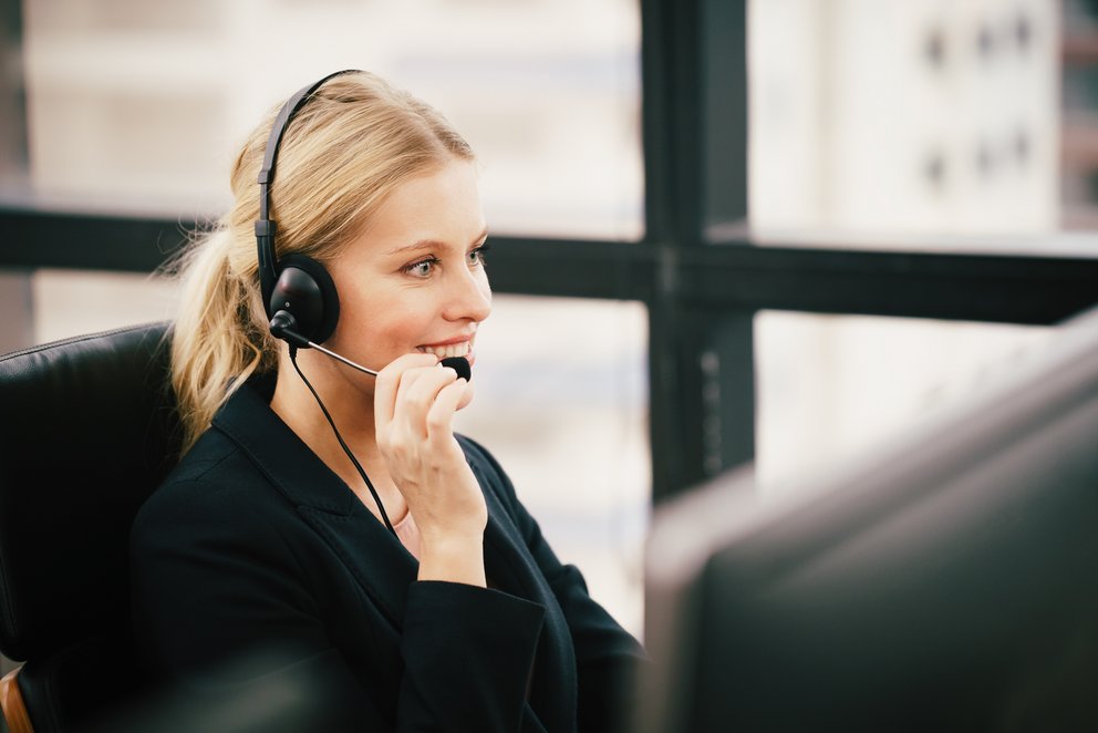Frau sitzt mit einem Headset. Frau sitzt mit einem Headset vor einem Computer und spricht