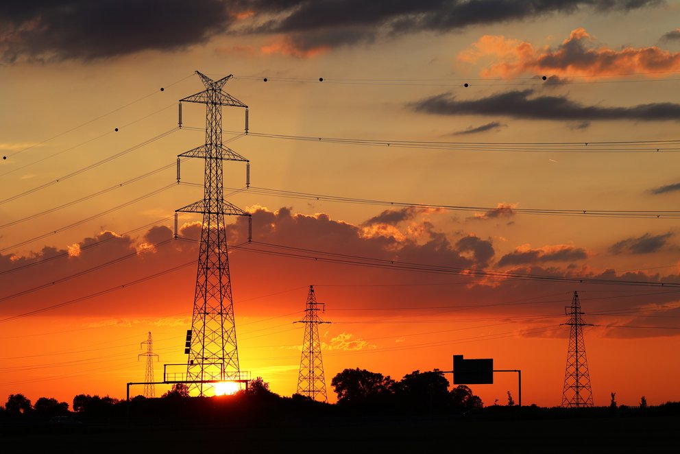Strommast und Leitungen vor einem Sonnenuntergang. AdobeStock_511385228. Strommast und Leitungen vor einem Sonnenuntergang.