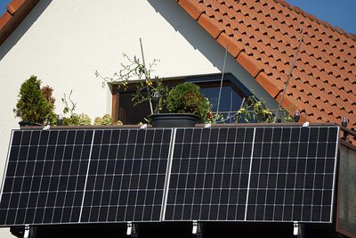 Ein Balkonkraftwerk an einem weiß verputztem Haus mit rotem Dach.