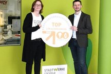 annete Dirks und Thomas Abels halten TOP-Lokalversorger-Siegel zwischen sich