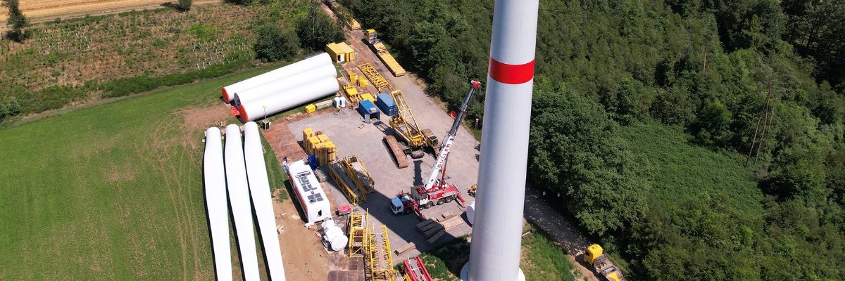 Aufbau eines Windkraftwerks, mit einer Windturbine und den Bauteilen in der Nähe, die für die Montage bereitgestellt werden.