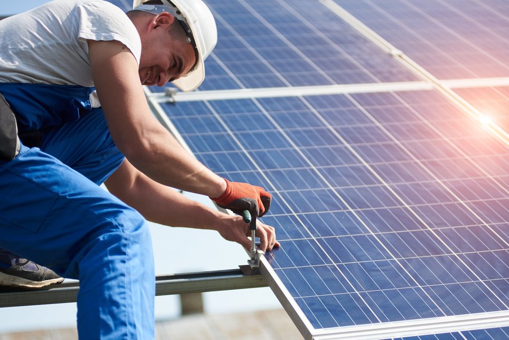 Das Bild zeigt einen Arbeiter, der ein Solarpanel auf einem Dach installiert.