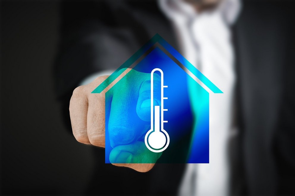 Haus-Symbol mit Thermometer in der Hand Hand, die ein Symbol eines Hauses mit einem Thermometer in der Mitte hält.