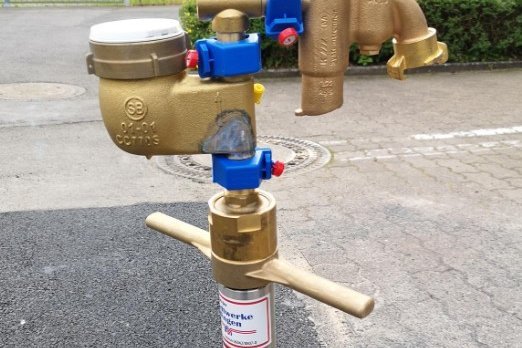 Wasserzähler und Ventile in Bodeninstallation. Das Bild zeigt einen Wasserzähler mit Anschlüssen, der in einem Bodenanschluss installiert ist.