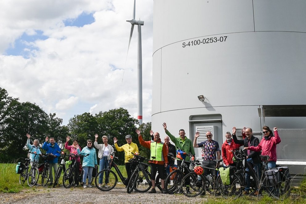 Gruppe von Radfahrer/innen vor dem Turm eines Windrads. 