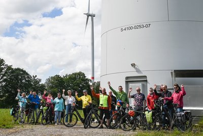 Gruppe von Radfahrer/innen vor dem Turm eines Windrads. 