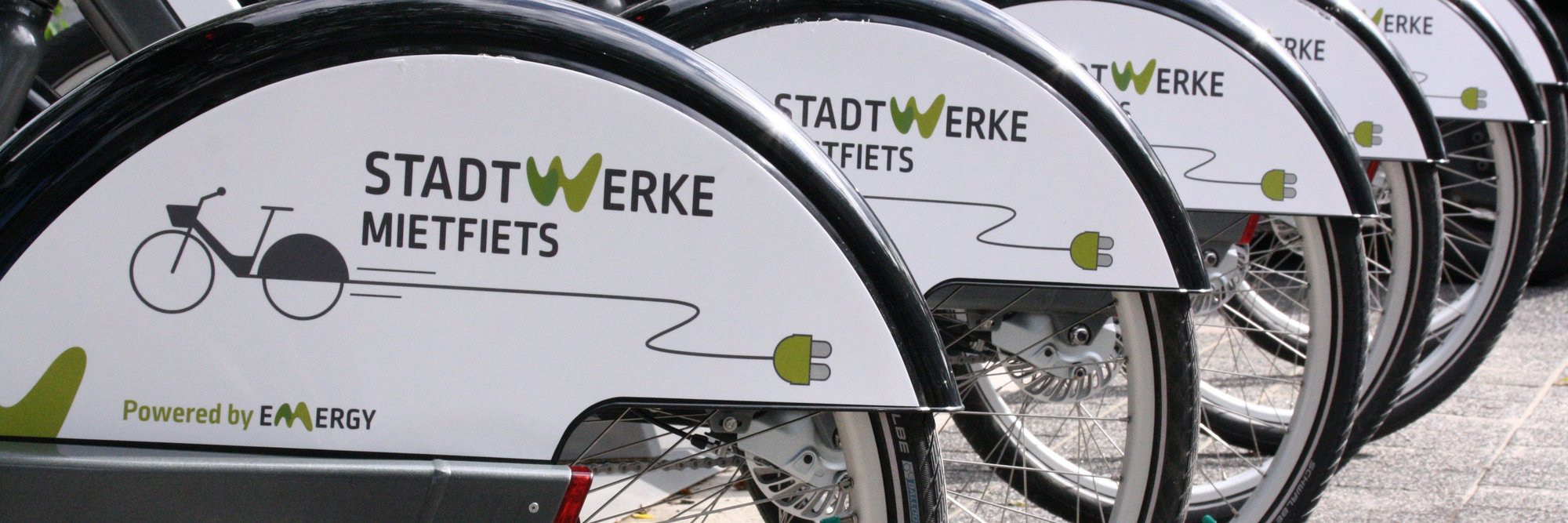 Stadtwerke-Fahrradverleih im öffentlichen Bereich. Eine Reihe von Fahrrädern, die Teil eines öffentlichen Verleihsystems zu sein scheinen, mit einem klar sichtbaren "Stadtwerke" Logo.