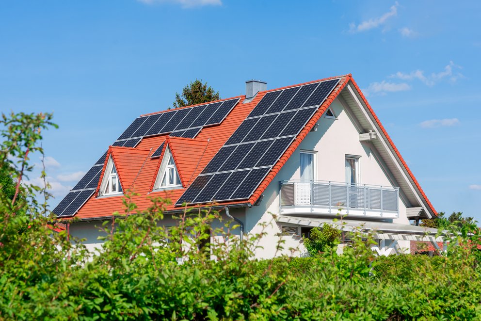 Haus mit rotem Satteldach und Solarpanels. Das Bild zeigt ein Haus mit einem roten Satteldach, das mit Solarpanels ausgestattet ist.