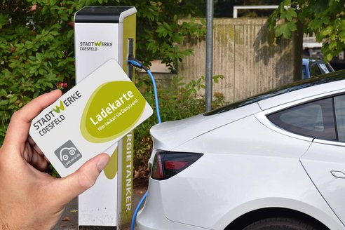 Jemand hält eine Ladekarte in der Hand, während er sich einem Elektroauto nähert.