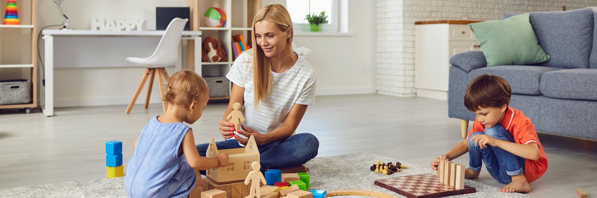 Mutter spielt mit Kindern im modernen Zimmer. Das Bild zeigt eine Mutter, die zusammen mit ihren zwei Kindern auf dem Boden eines hellen, modernen Zimmers spielt.