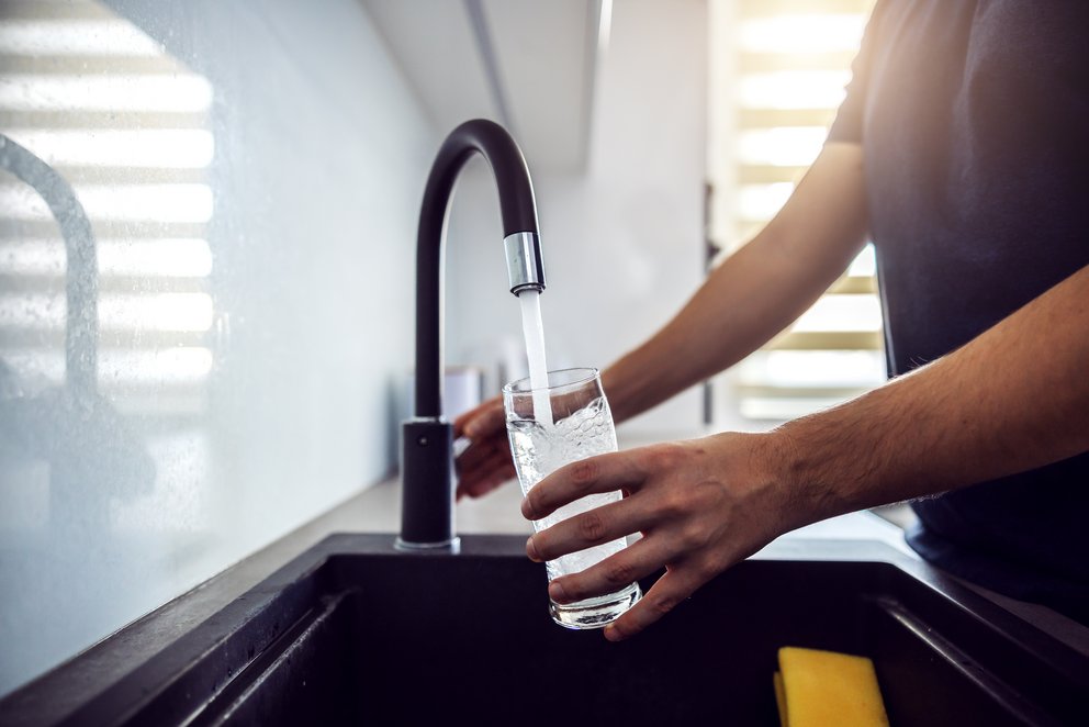 Person füllt Glas mit Wasser aus modernem Hahn. eine Person, die gerade Wasser aus einem modernen Wasserhahn in ein Glas gießt.
