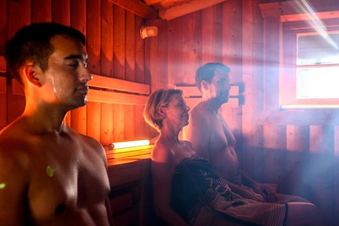 Eine Gruppe von Menschen entspannt in einem Saunaraum, umgeben von Holzverkleidung und dampfender Luft.