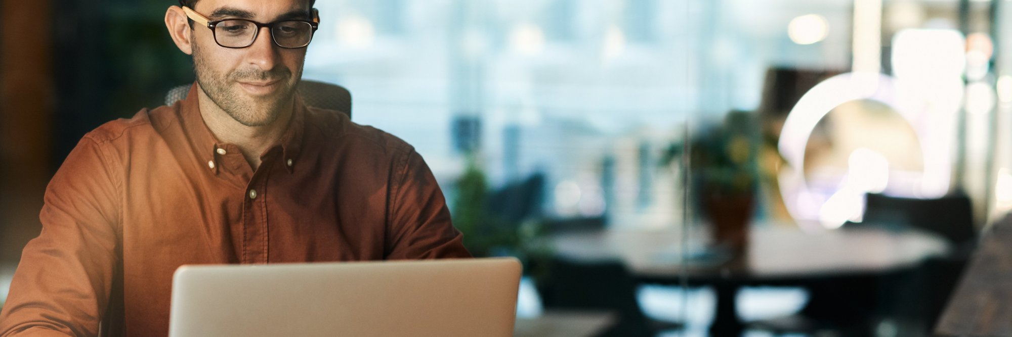 Ein Mann mit Brille sitzt am Tisch und schaut auf einen Laptop. Ein Mann mit Brille sitzt am Tisch und schaut auf einen Laptop.
