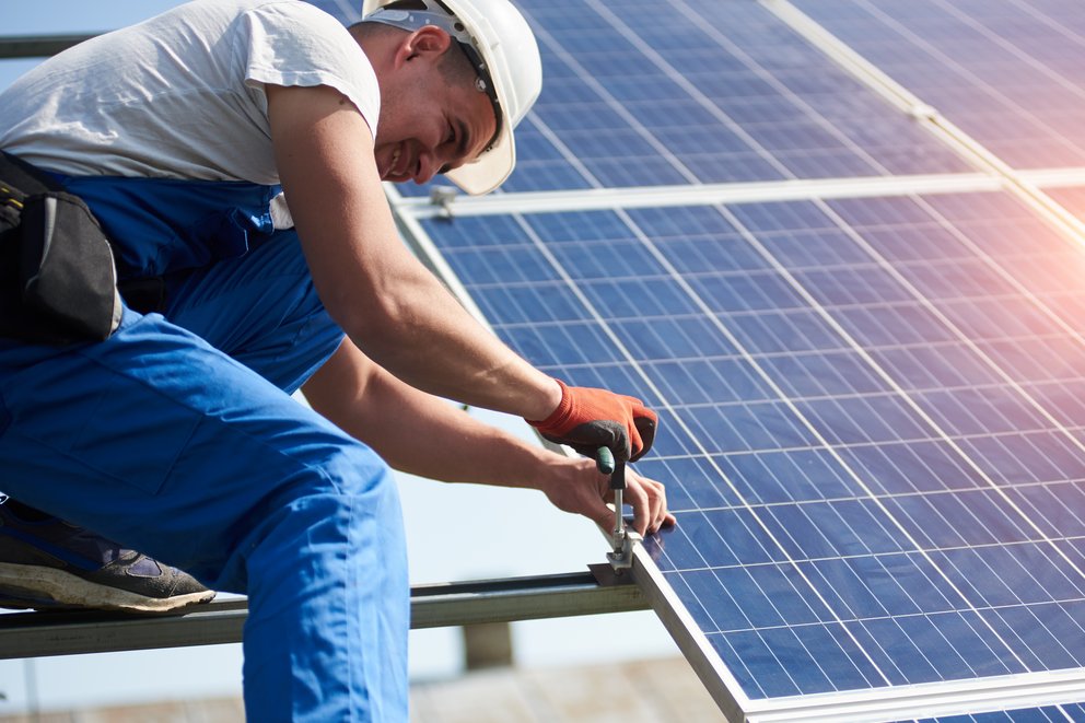 Das Bild zeigt eine Person, die auf einem Dach ein Solarpanel installiert.