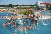 Ein weitläufiger Pool, gefüllt mit Menschen, die schwimmen und sich amüsieren, umgeben von Sonnenlicht und entspannter Atmosphäre.