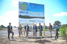 eine Gruppe von Personen, die ein Baustellenbanner für ein Windkraftprojekt präsentieren.